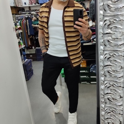 Homem com camisa de riscas castanhas, t-shirt branca, calças pretas e ténis brancos, selfie em loja