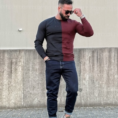 Homem com camisola preta e bordô de manga comprida, calças de ganga e ténis numa rua urbana