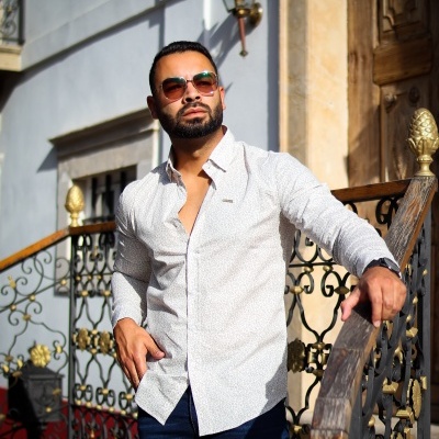 Homem com camisa branca padrão e óculos de sol junto a corrimão dourado
