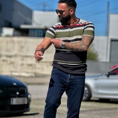 Homem com t-shirt de riscas coloridas, calças de ganga, óculos de sol e relógio em ambiente urbano