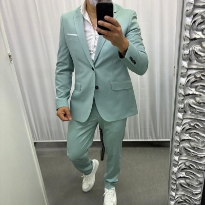 Homem com fato verde-menta e sapatilhas brancas a tirar selfie num espelho com moldura prateada num espaço interior.