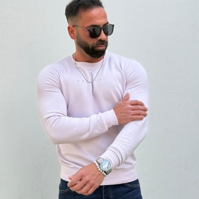 Homem com camiseta rosa claro, calças de ganga, óculos de sol e relógio