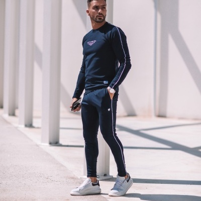 Conjunto desportivo masculino azul escuro com riscas brancas e ténis brancos em ambiente exterior