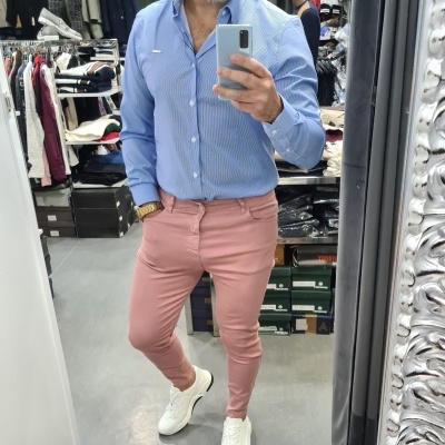 Homem de camisa azul clara e calças cor de rosa a tirar selfie em loja de roupas