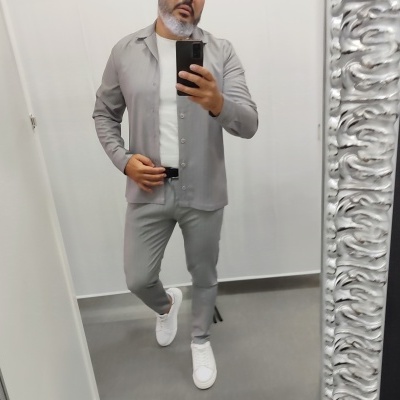 Homem com roupa cinzenta e branca a tirar selfie num espelho com moldura prateada