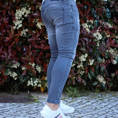 Pessoa de pé com calças de ganga cinzentas e sapatilhas brancas junto a plantas