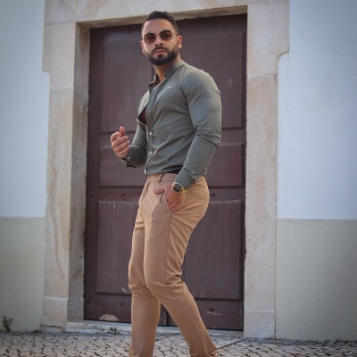 Homem com camisa verde e calças bege junto a porta de madeira