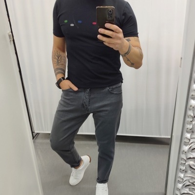 Homem com t-shirt preta, jeans cinza e ténis brancos a tirar selfie num espelho