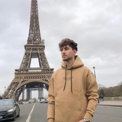 Homem com hoodie bege e jeans em frente à Torre Eiffel