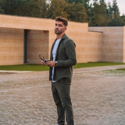 Homem com conjunto verde escuro, t-shirt branca e sapatilhas brancas em calçada