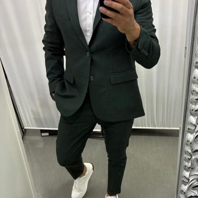 Homem a vestir fato verde escuro com camisa branca e sapatilhas brancas a tirar selfie num espelho