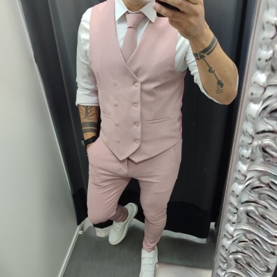 Homem vestido com fato cor de rosa claro, camisa branca e ténis brancos, tirando selfie num espelho com moldura prateada