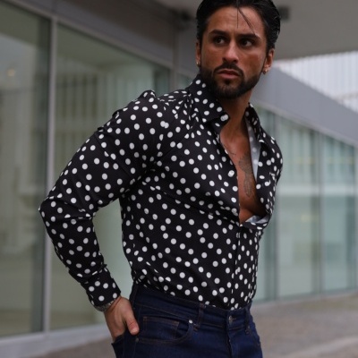 Homem com camisa preta de bolinhas brancas e calças de ganga azuis escuras ao ar livre