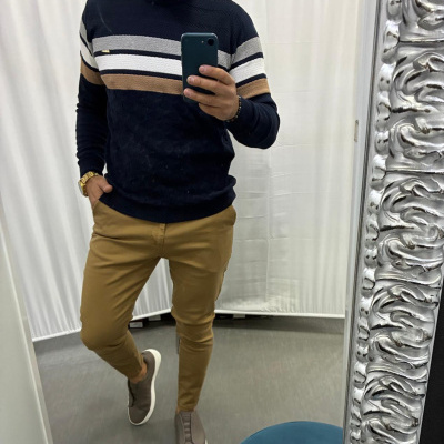 Homem a vestir camisola preta com riscas e calças bege a tirar selfie num espelho decorativo prateado