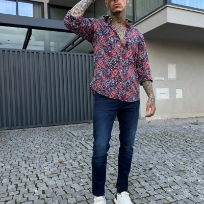 Homem com camisa paisley, jeans e ténis brancos em ambiente urbano