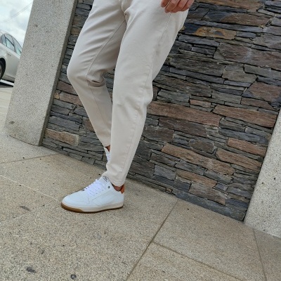 Homem com sapatilhas brancas e calças bege junto a muro de pedra
