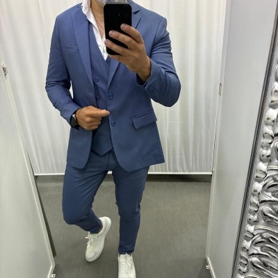Homem vestido com fato azul e ténis brancos em frente a espelho