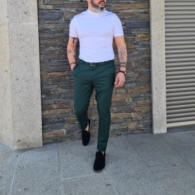 Homem com t-shirt branca, calças verdes, sapatos pretos em ambiente urbano