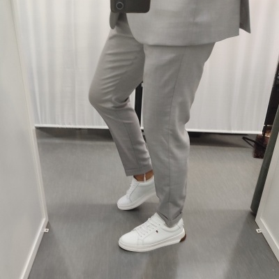 Calças de fato cinza com sapatos desportivos brancos numa sala interior.