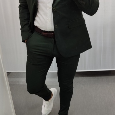 Homem com fato verde escuro, camisa branca e sapatilhas brancas a tirar selfie