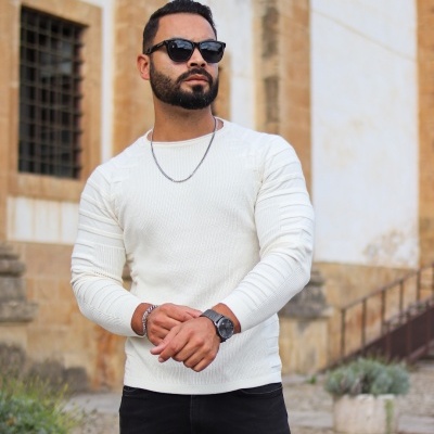 Homem com camisola branca de malha, calças pretas e acessórios prateados e pretos ao ar livre