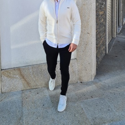 Homem com camisola branca e calças pretas num ambiente urbano.