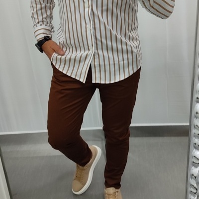 Homem com camisa às riscas castanhas, calças castanhas e sapatilhas bege frente a espelho