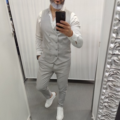 Homem vestindo colete e calças cinza claro, camisa branca e sapatilhas brancas em loja