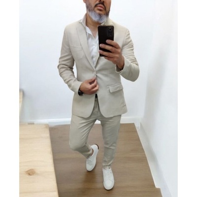 Homem de fato bege claro com camisa branca e ténis brancos numa divisão interior