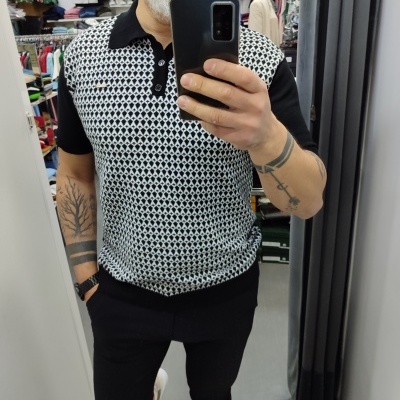 Homem com polo preta e padrão geométrico a tirar selfie em loja de roupa