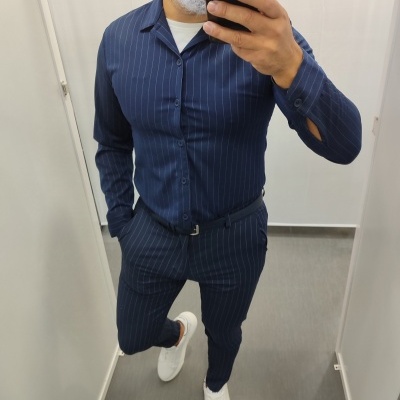 Conjunto de fato azul riscado com camisa e calças ajustadas, cinto preto e sapatilhas brancas numa cabine de prova
