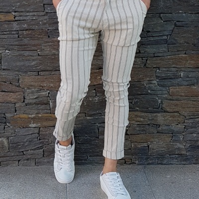 Calças bege riscas verticais com sapatilhas brancas junto a parede de pedra