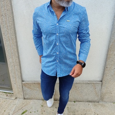 Homem com camisa azul padrão floral, calças de ganga e sapatilhas brancas