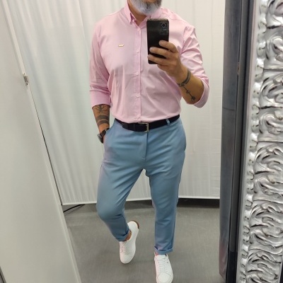 Homem com camisa rosa, calças azuis, cinto preto e sapatilhas brancas num espelho