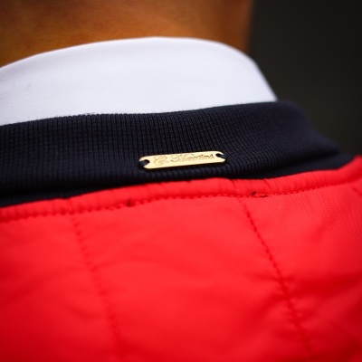 Gola de jaqueta vermelha com gola azul escura e placa metálica dourada