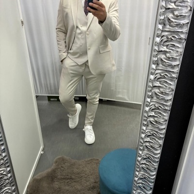 Homem a usar fato bege claro com gravata roxa e sapatilhas brancas, a tirar selfie num espelho com moldura prateada