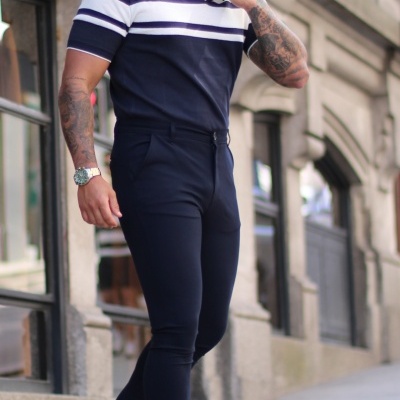 Homem com polo azul-marinho e riscas brancas e calças justas azul-escuras em rua urbana