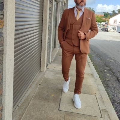 Homem com fato castanho, camisa branca, gravata castanha clara e sapatos brancos a caminhar junto a loja