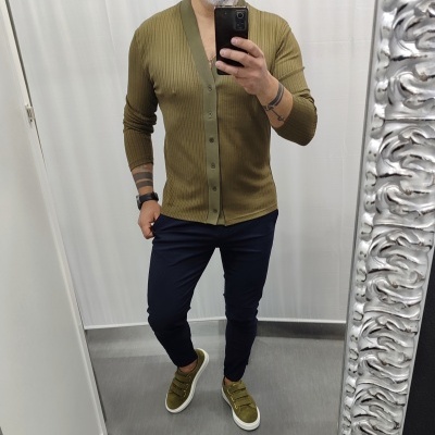 Homem com cardigan verde, calças azuis e sapatilhas verdes a tirar selfie em espelho com moldura prateada