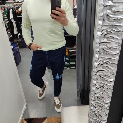 Pessoa em provador com sweatshirt verde claro, calças de ganga azul rasgadas e sapatilhas castanhas e brancas.