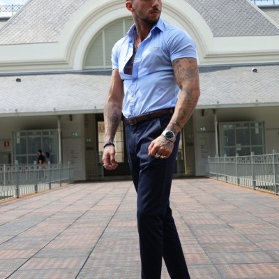 Homem com camisa azul clara, calças pretas e sapatos azul claro posando ao ar livre