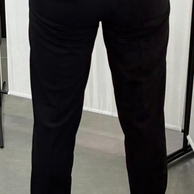 Calças pretas com bolsos traseiros de aba e botão usadas por uma pessoa com camisa branca e ténis brancos