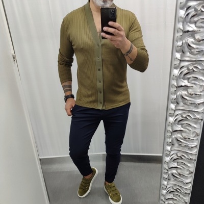 Homem com cardigan verde oliva, calças azul-escuras e ténis verdes a tirar selfie em espelho decorado