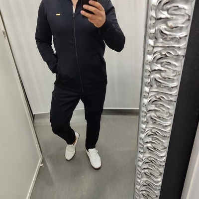 Homem com conjunto desportivo preto e ténis brancos a tirar selfie em espelho num provador