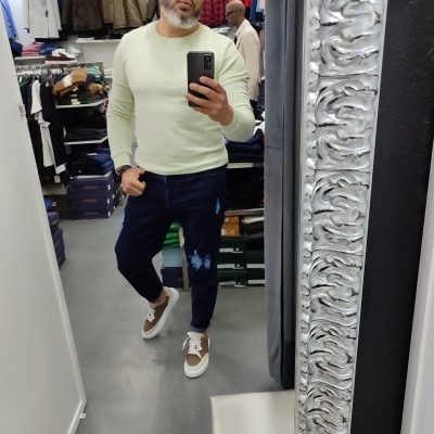 Homem com camisola bege clara e calças de ganga azuis escuras numa loja de roupas