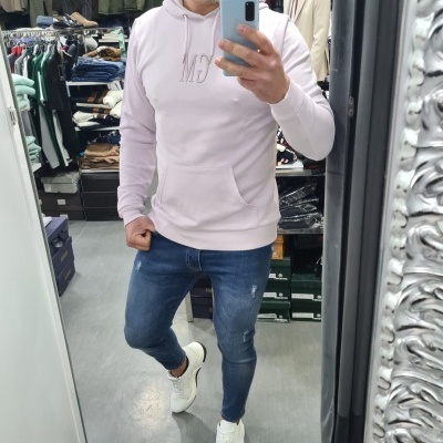 Homem veste hoodie rosa claro, jeans azul e sapatilhas brancas numa loja de roupa.