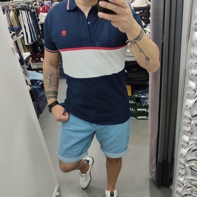 Homem a usar polo azul escuro com faixa branca e calções de ganga azul claro num provador