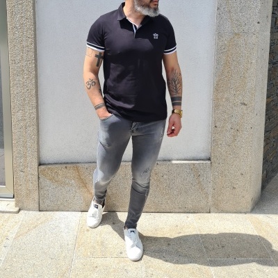 Homem com polo preta, calças de ganga cinza e ténis brancos em ambiente urbano