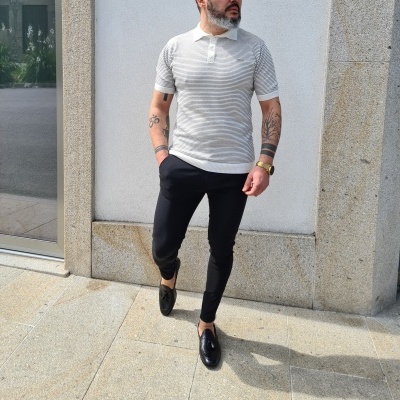 Homem com polo cinza listrada, calças pretas e sapatos pretos numa rua urbana