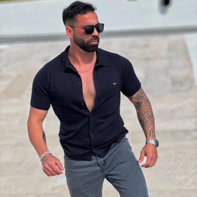 Homem com camisa preta e óculos de sol em exterior com piso cinzento